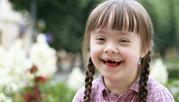 A young girl with down syndrome is hanging out in a garden.