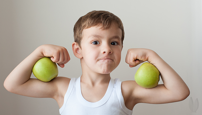 A young boy is flexing and pretending the apples are his muscles.