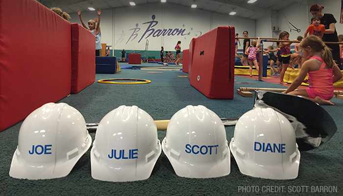 Four hardhats are lined up with the name of each coach on them.