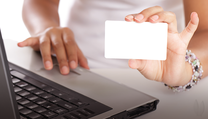 A woman is typing on her computer holding up a blank card.