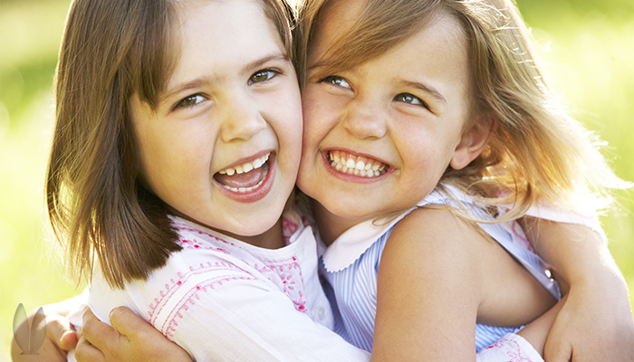Two smiling girls are hugging each other outside on a nice sunny day.