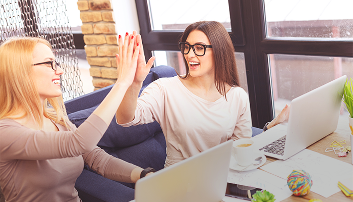 Two working women are high fiving in a coffee shop.