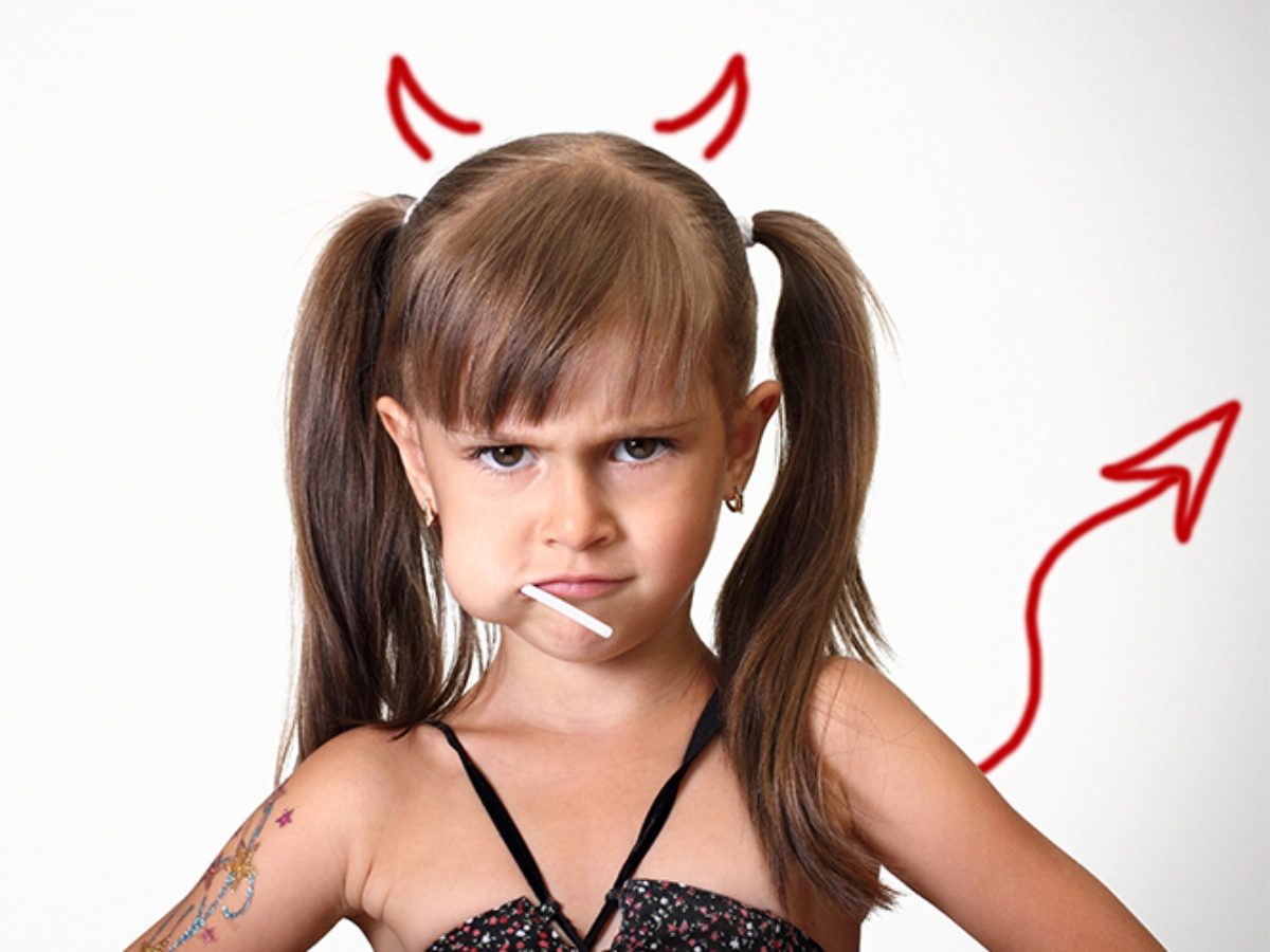 An angry girl with devil horns is eating a lollipop.