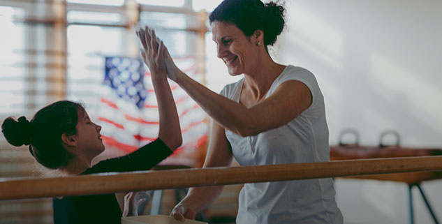 A gymnastics instructor and a gymnast are high fiving.