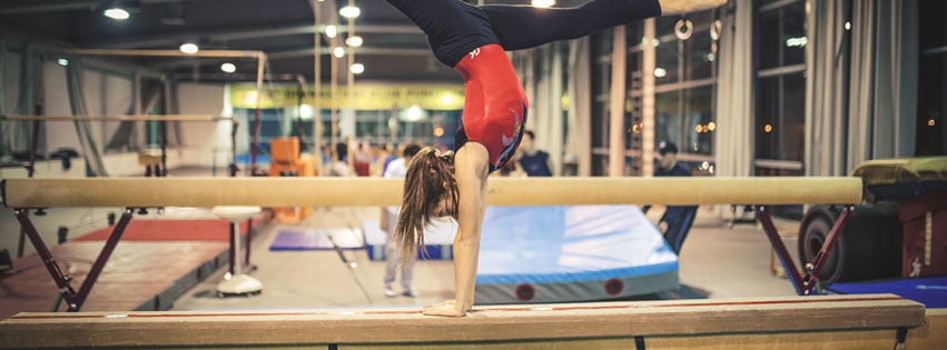 A gymnast is doing a handstand on the balance beam.