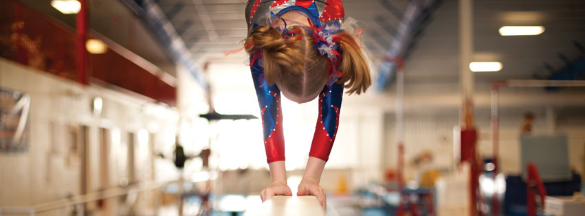 Young girl does a handstand on the balance beam creating an ideal experience for parents and students at childrens gym