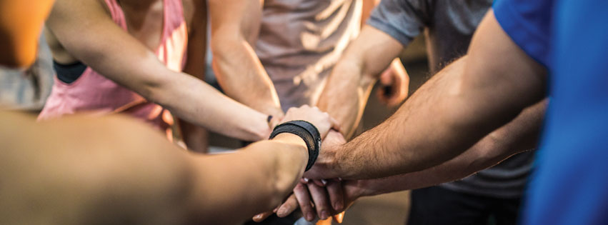 gym staff holding hands together as a sign of cooperation and staffing the right people for your kids' gym