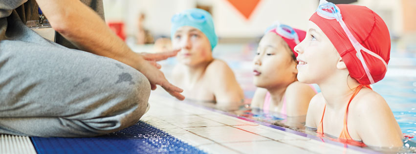 young swim students taking advice from coach to prevent swimmer's ear