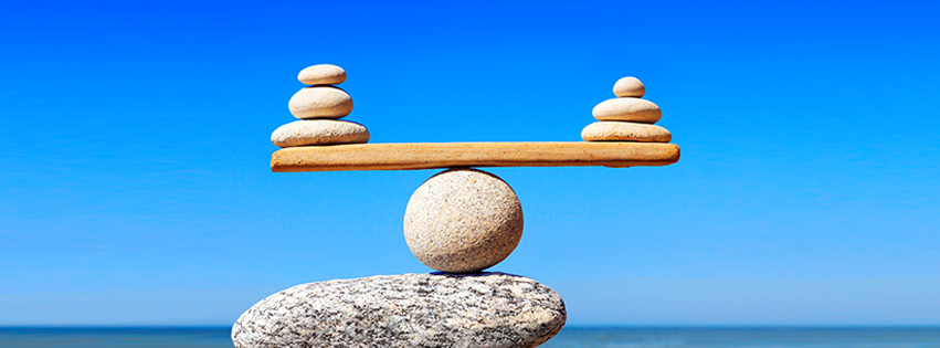 Two piles of flat rocks balancing on a wooden plank that is balancing on a round rock.