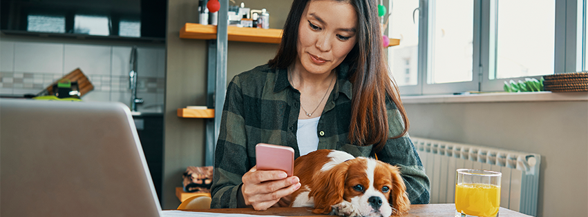 A woman is texting her friends and petting her dog while working remotely.