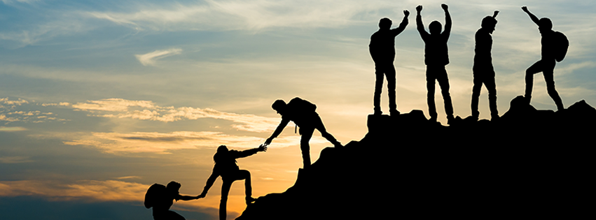 A group of hikers reaching the top of a mountain at sun set.