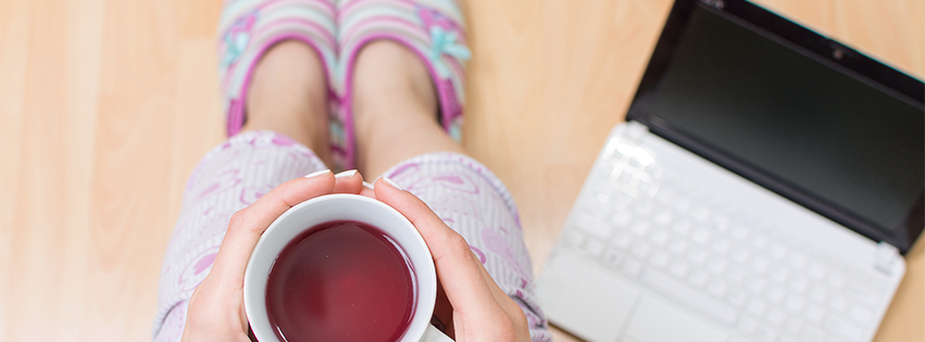 A woman wearing pajamas is drinking her coffee while working remotely.