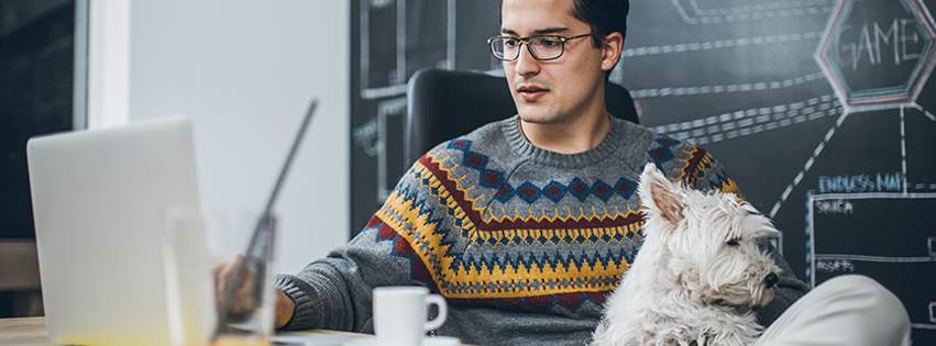 A man his working remotely while holding his dog.