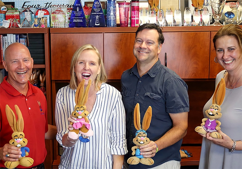 mark, tracy, mike, jorine holding bunny in front of awards case