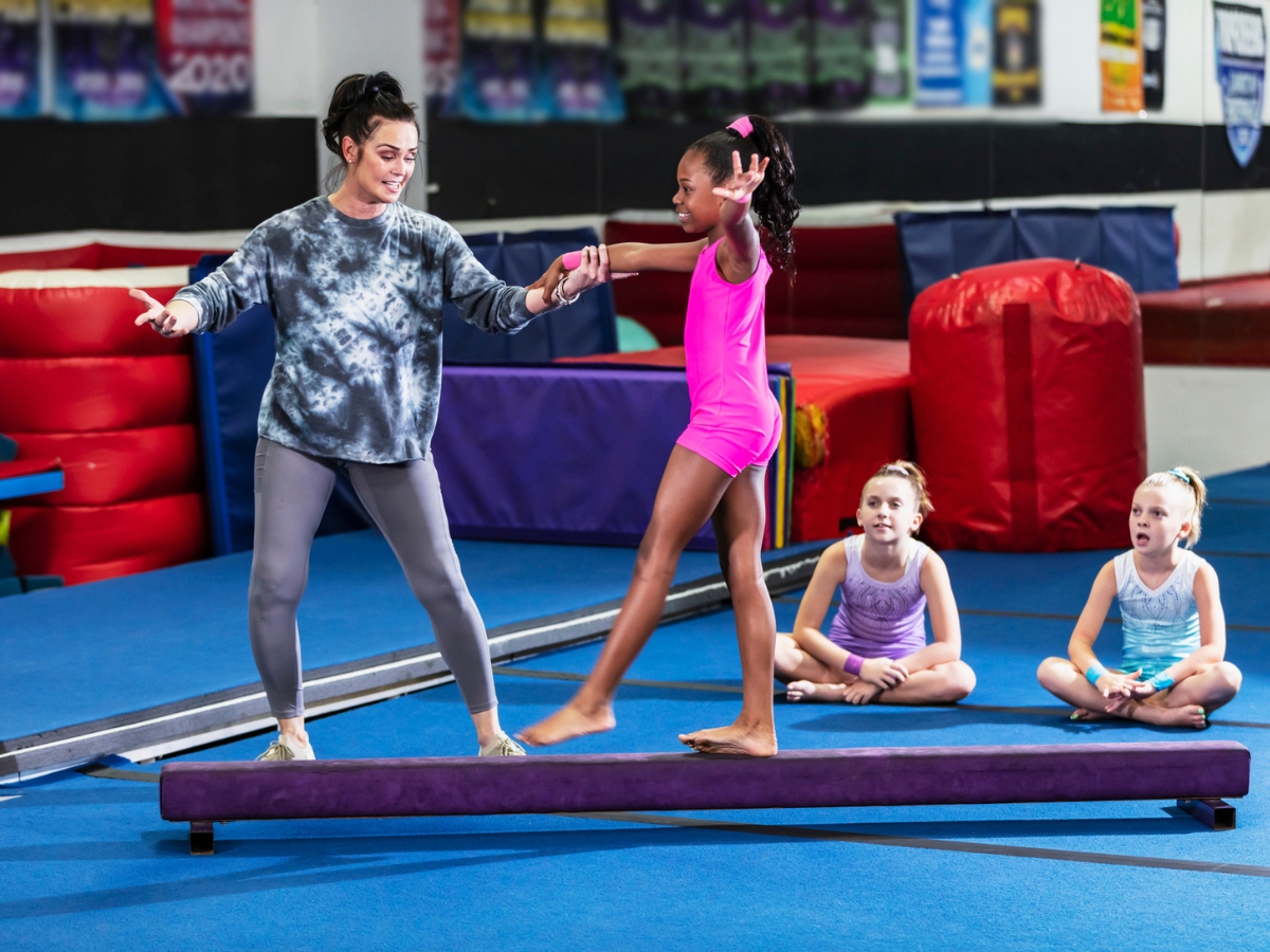 A gymnastics coach helps her student in a balancing exercise